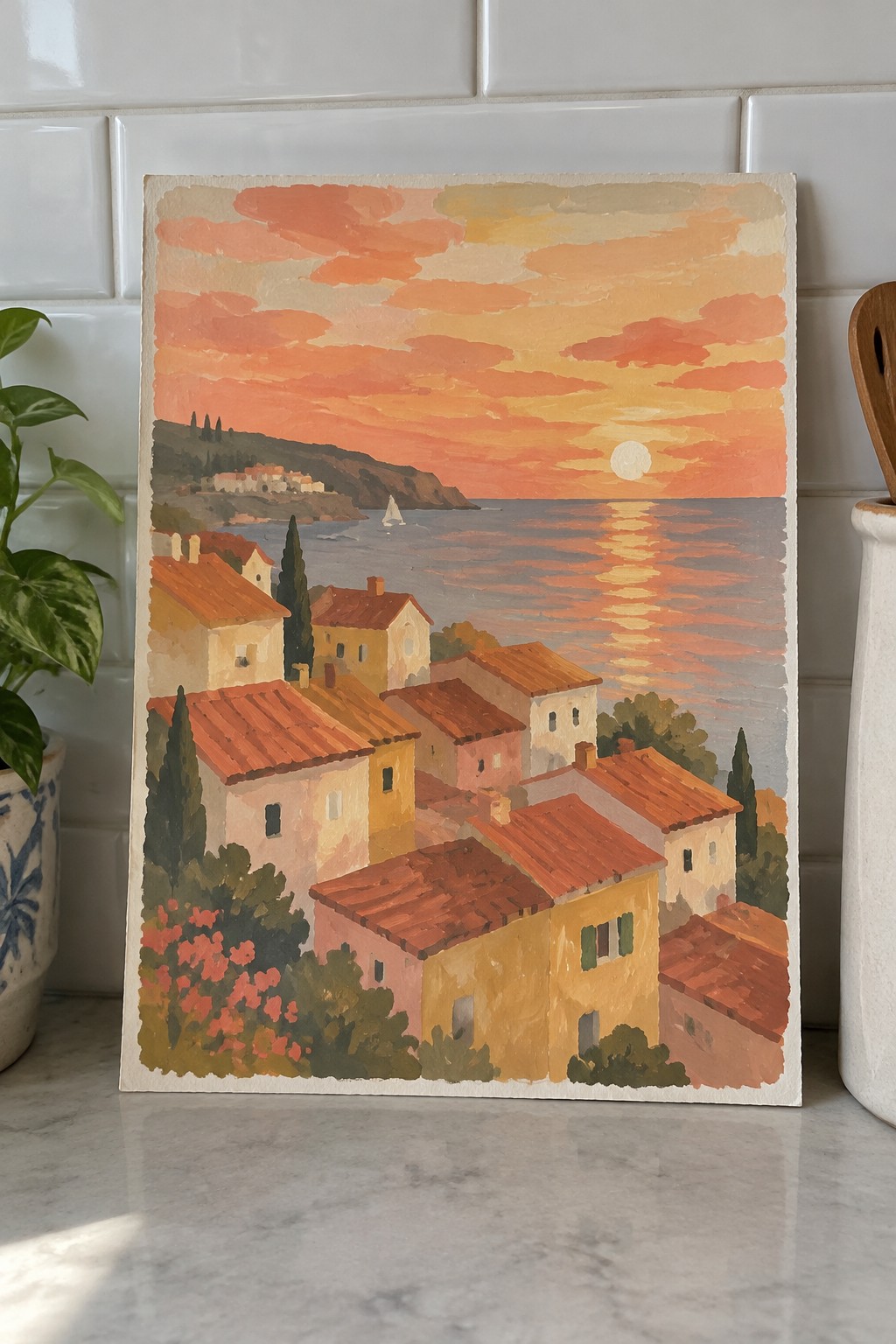 Coastal village at sunset with terracotta roofs, sailboat on glowing sea under orange sky