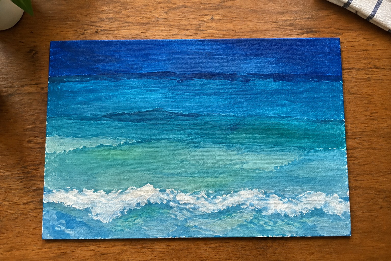 Seascape painting with layered blues, turquoise, and white waves on wood table
