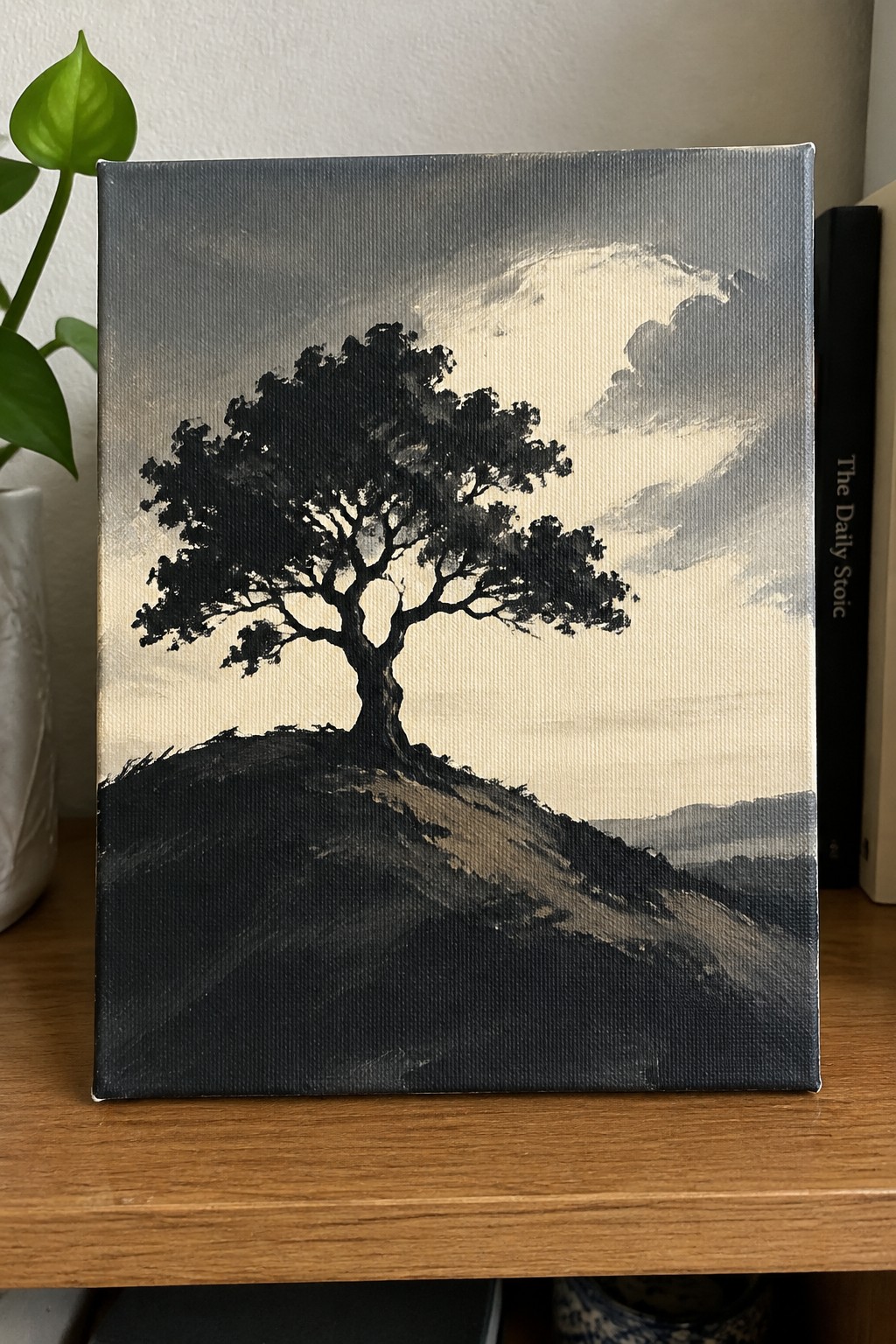Monochrome painting of lone tree silhouetted on dark hill under dramatic cloudy sky