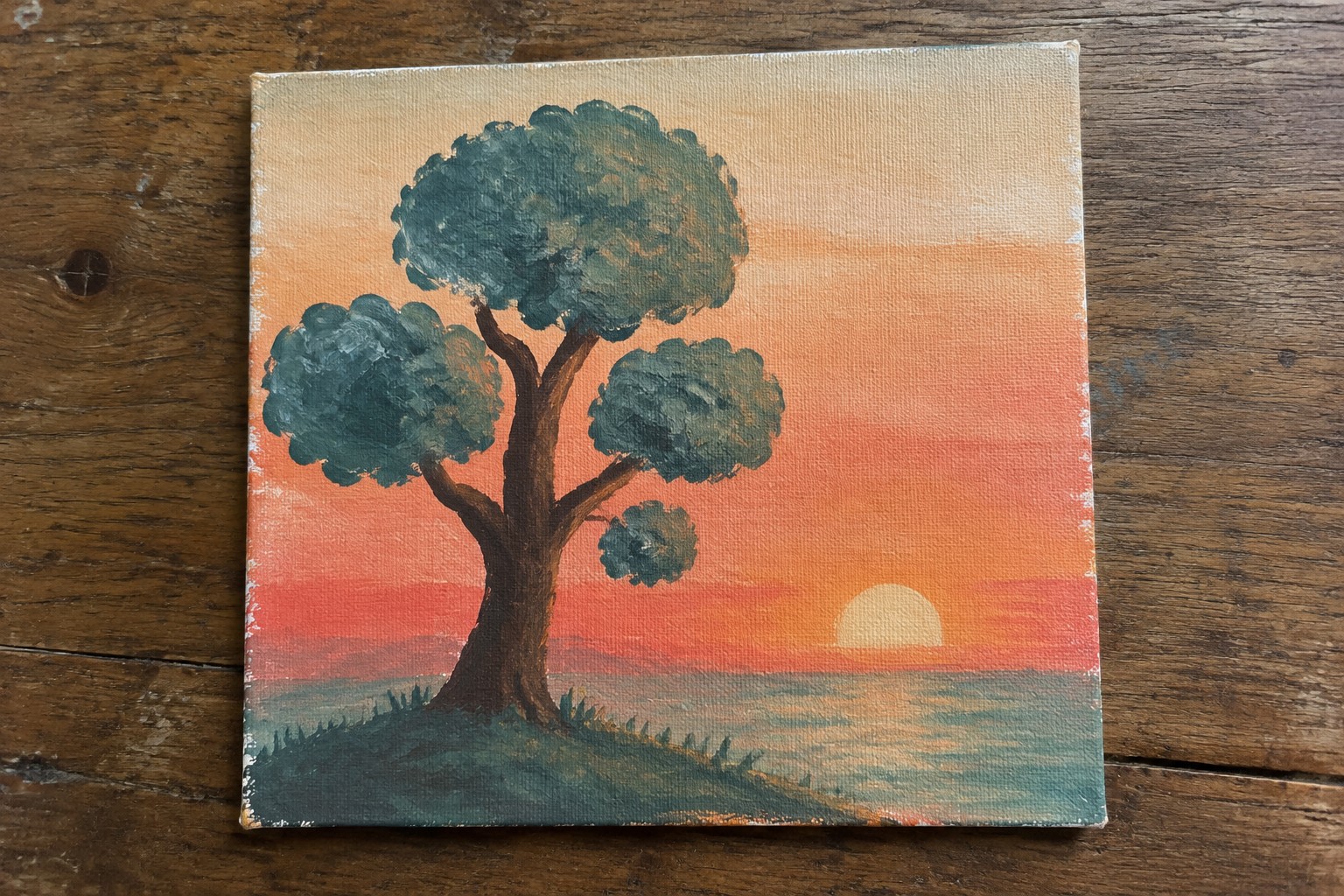 Tree with green foliage against orange-pink sunset over water on canvas