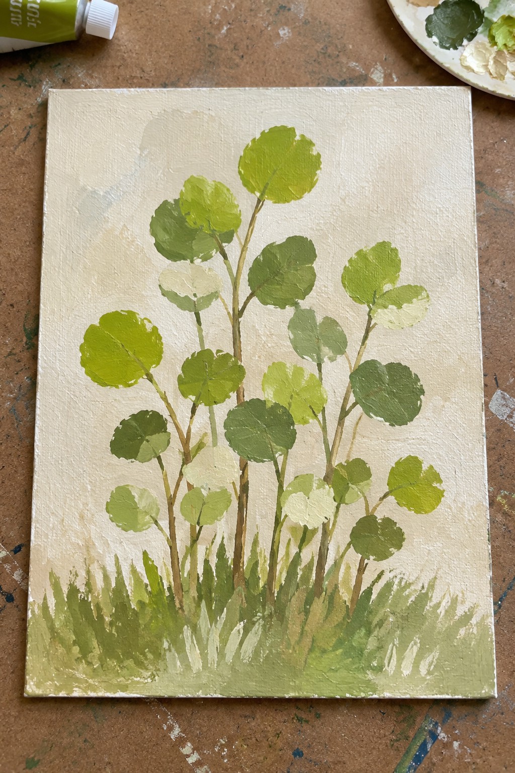 Canvas painting of round green leaves on stems above grassy base with art supplies nearby