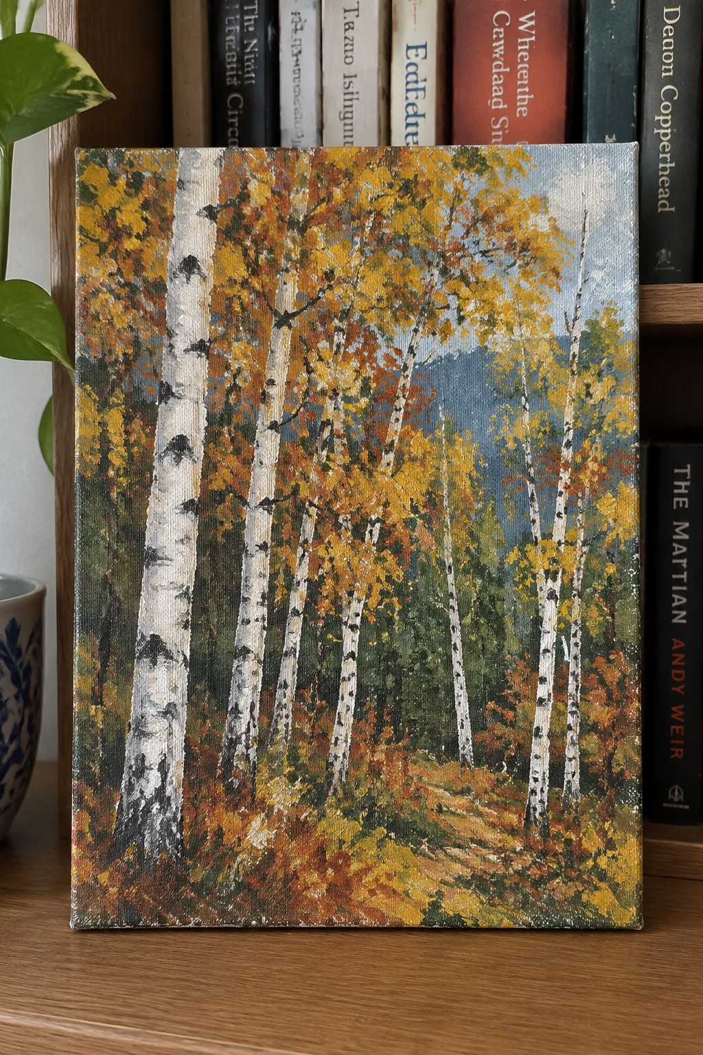 Autumn birch forest painting on canvas against books and potted plant