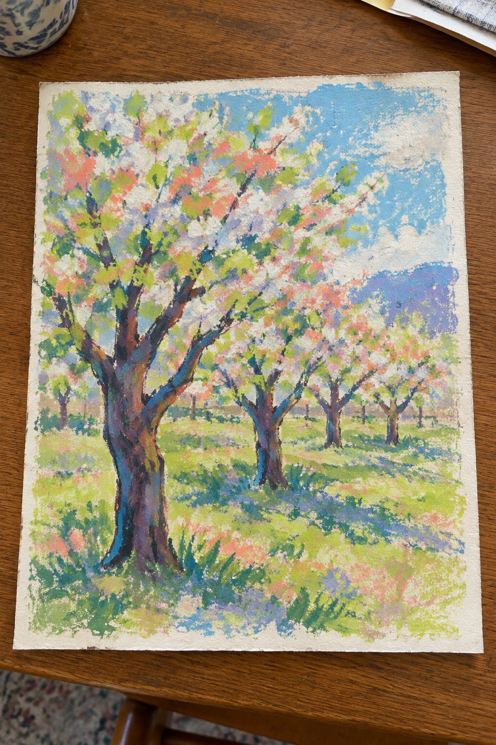 Vibrant painting of pink-blossomed trees in a green meadow under blue sky