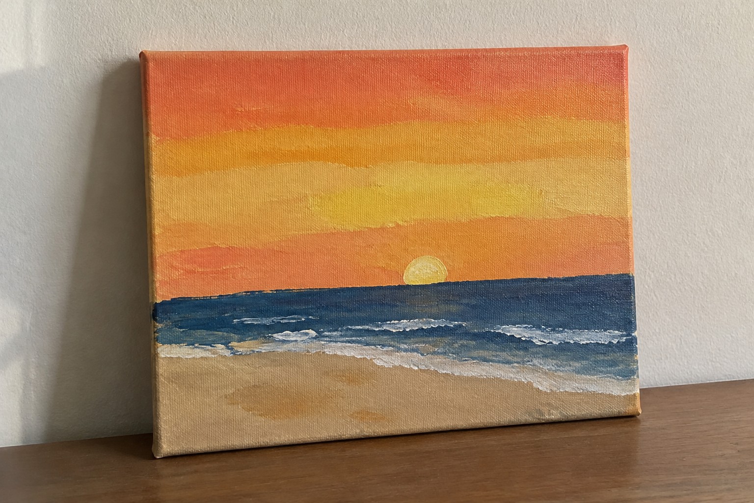 Seascape painting of sunset with orange sky, yellow sun, blue waves, and sandy beach