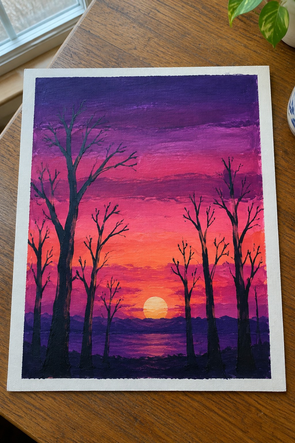 Acrylic painting of a sunset gradient from purple to orange with a yellow sun low on the horizon and black bare tree silhouettes in front of distant hills.