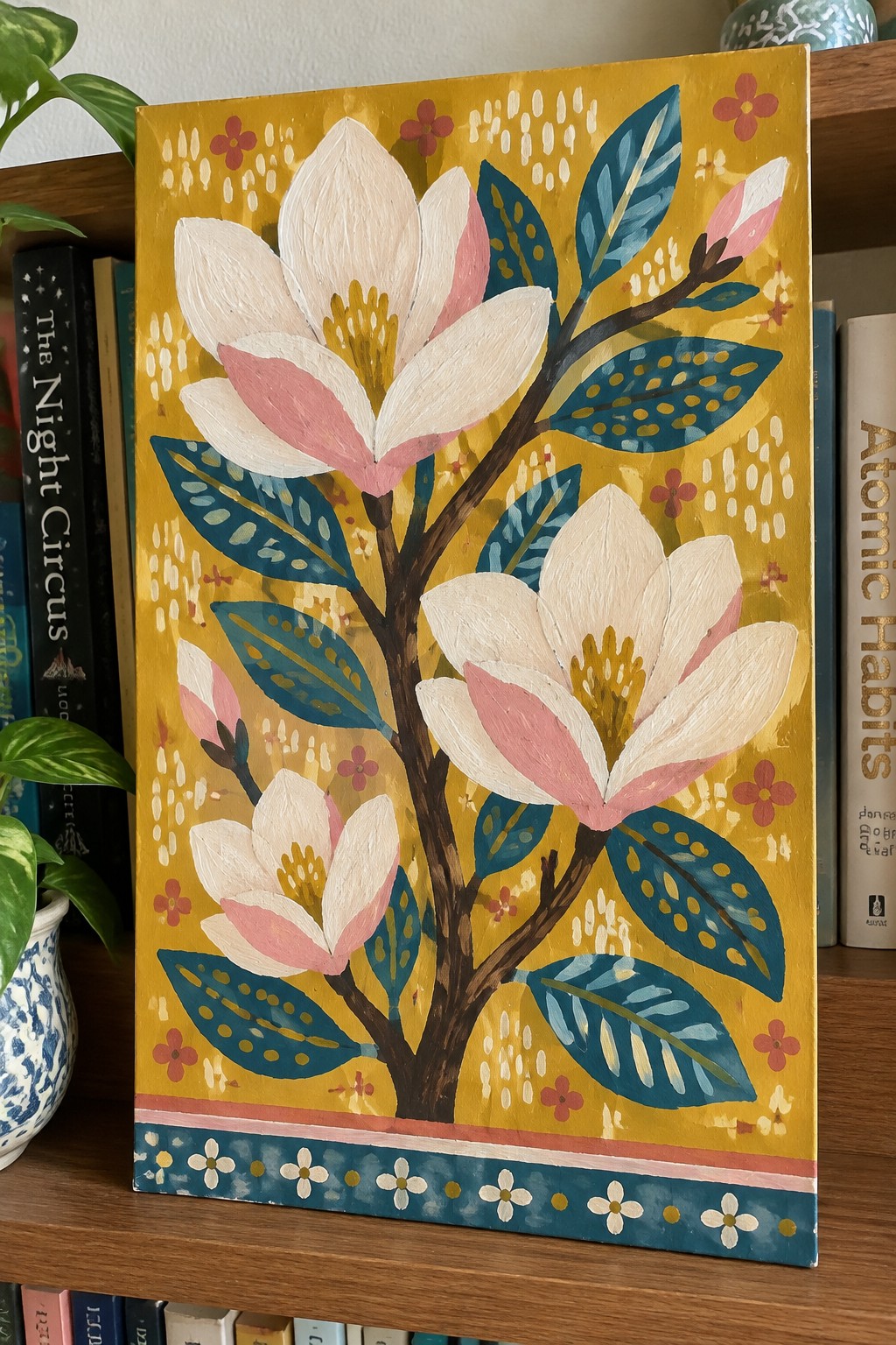 Vibrant painting of white magnolias with pink centers and blue dotted leaves on yellow background