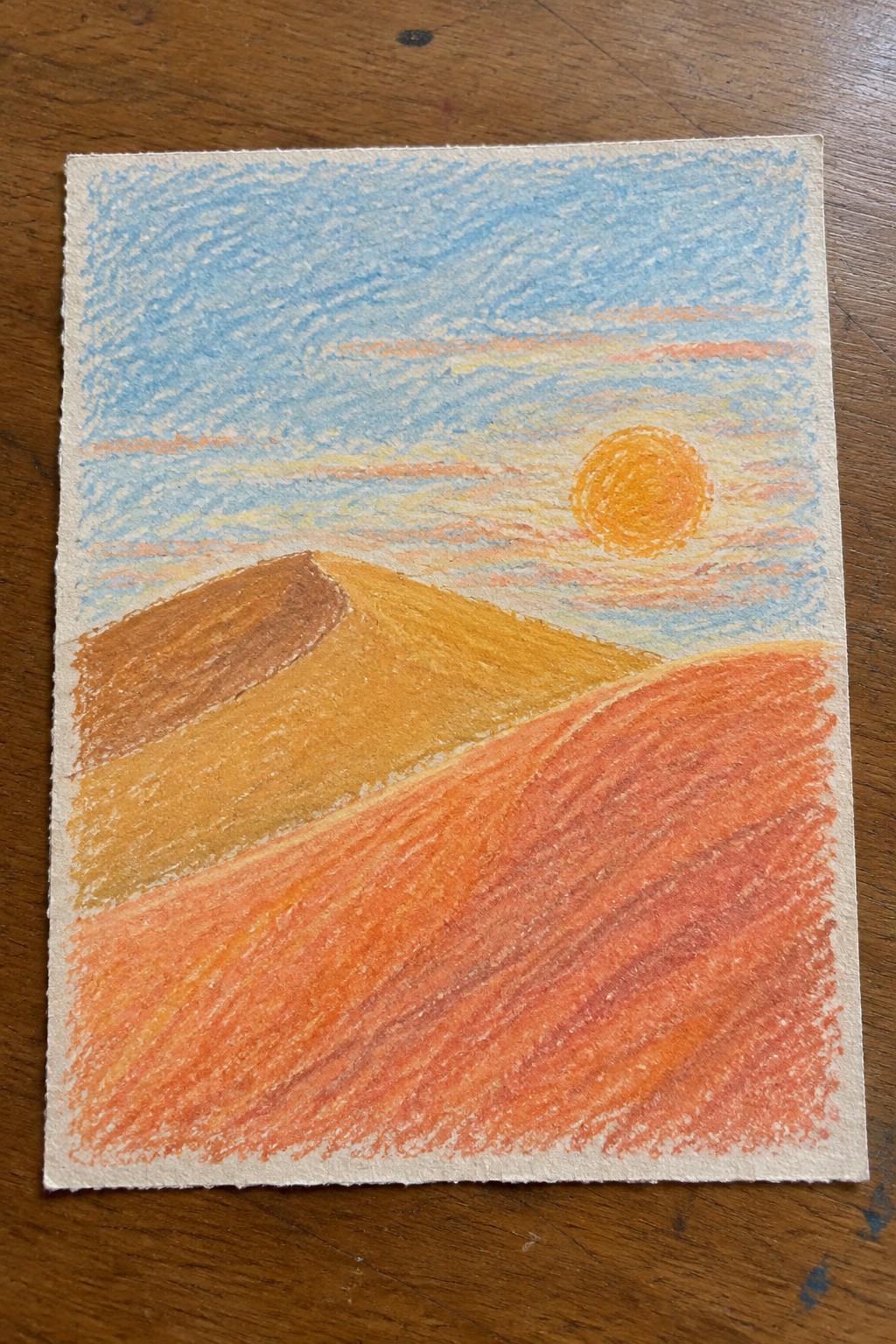 Vibrant crayon drawing of layered orange dunes beneath a bright sun in blue sky