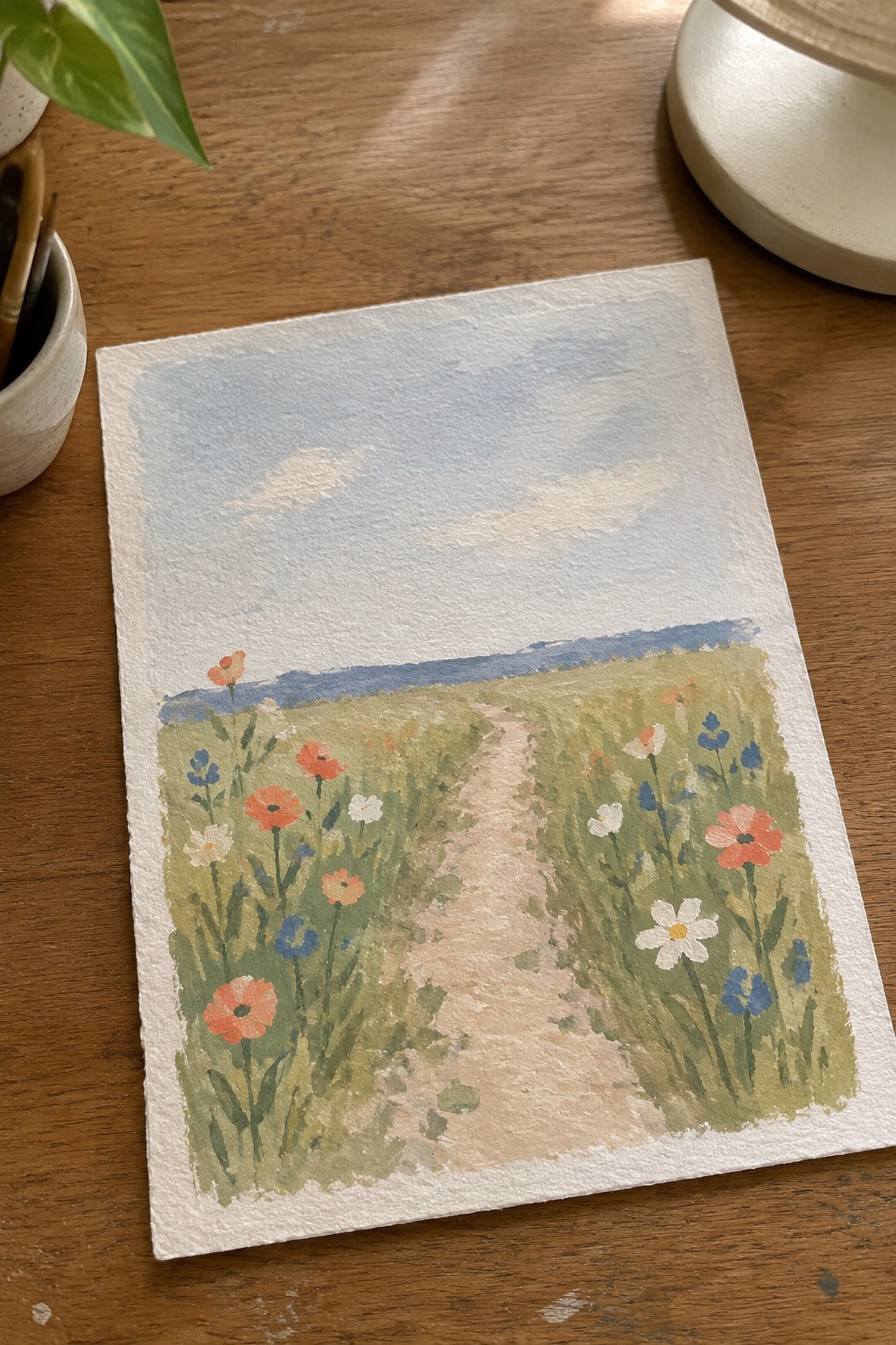 Watercolor of a winding path through a wildflower meadow under a cloudy blue sky
