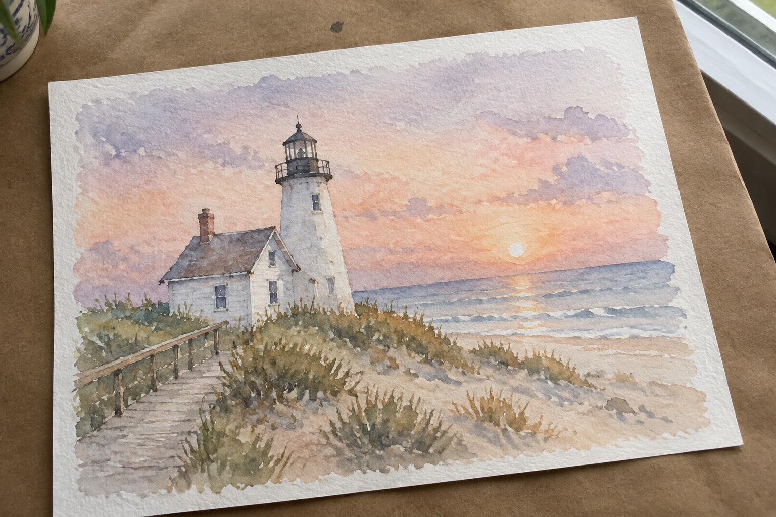 Watercolor of white lighthouse with house on grassy dunes overlooking ocean at sunset