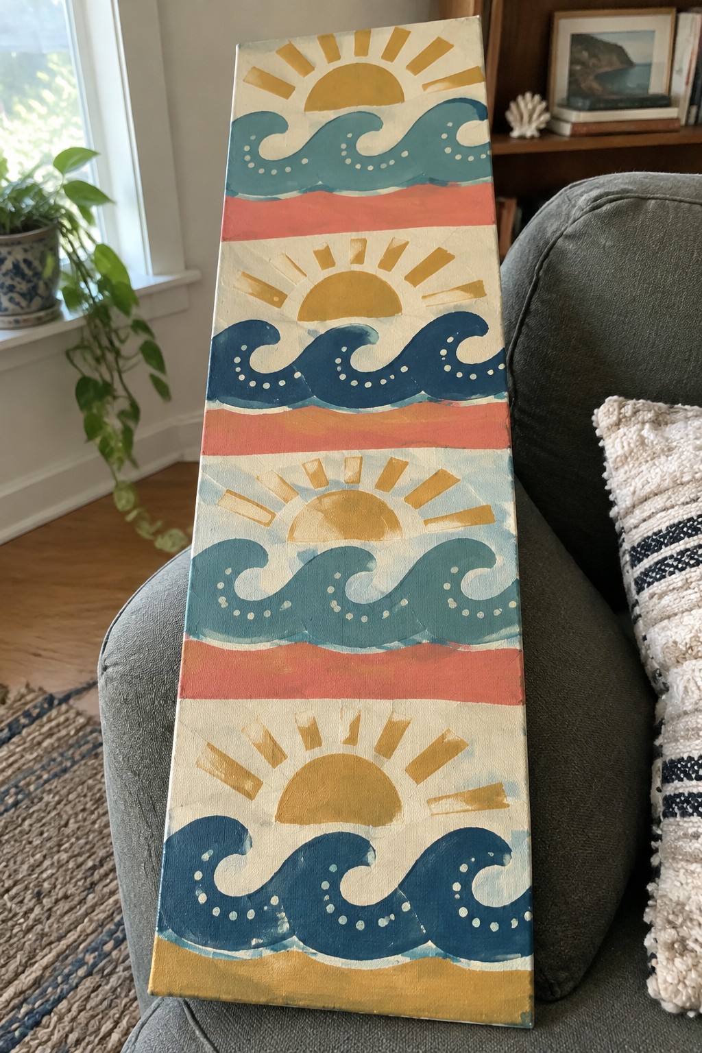 Colorful vertical canvas with suns, waves, and stripes leaning on gray couch.