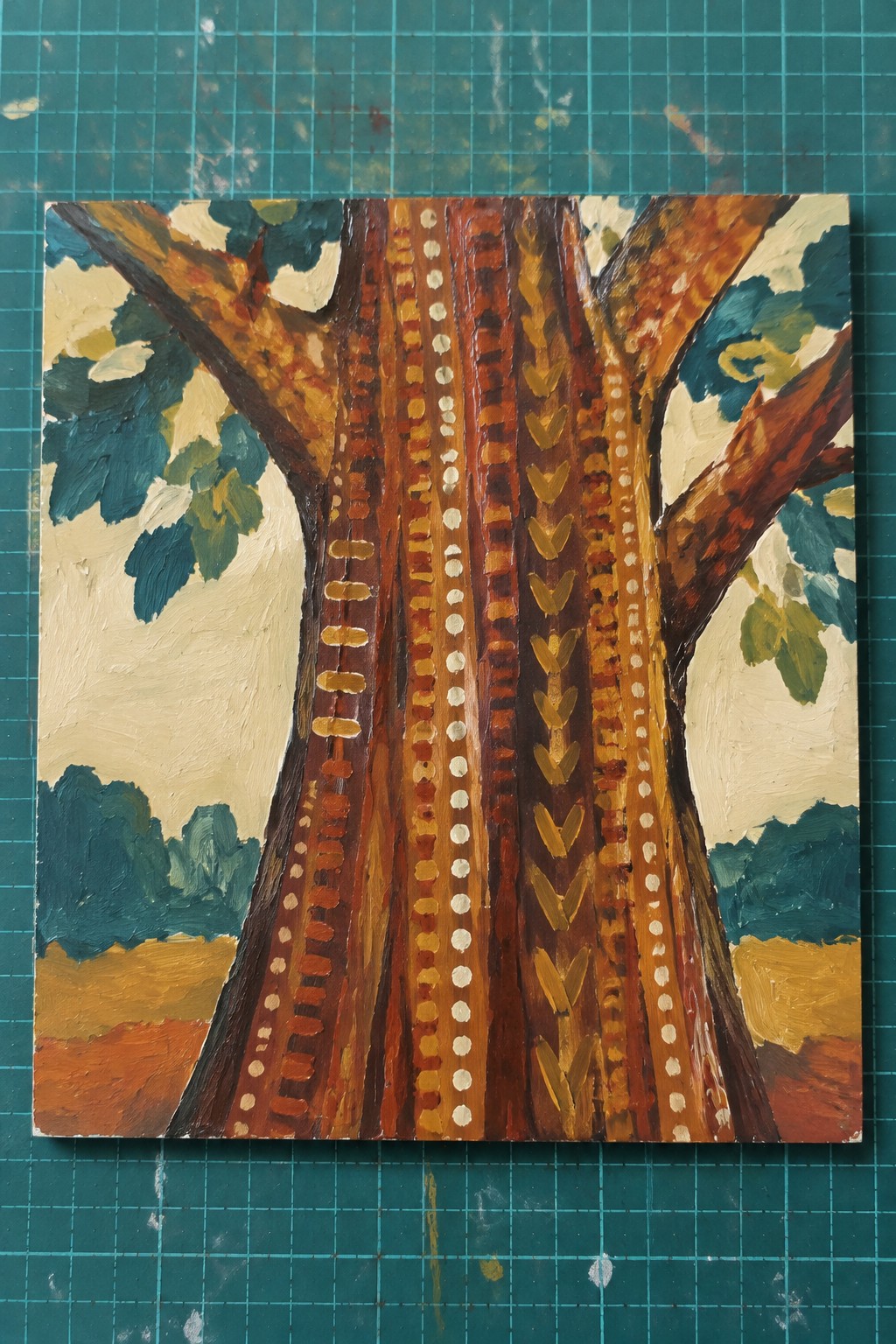 Impasto painting of tree trunk with dotted chevron patterns on green cutting mat.