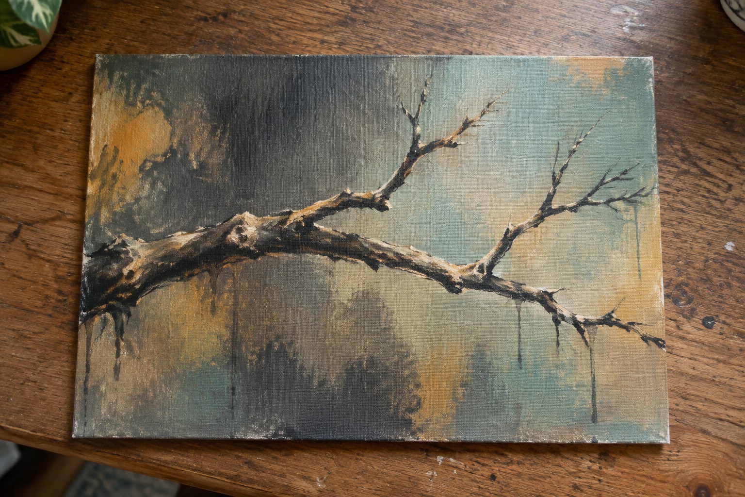 Moody painting of a gnarled bare branch with yellow drips on wooden table.