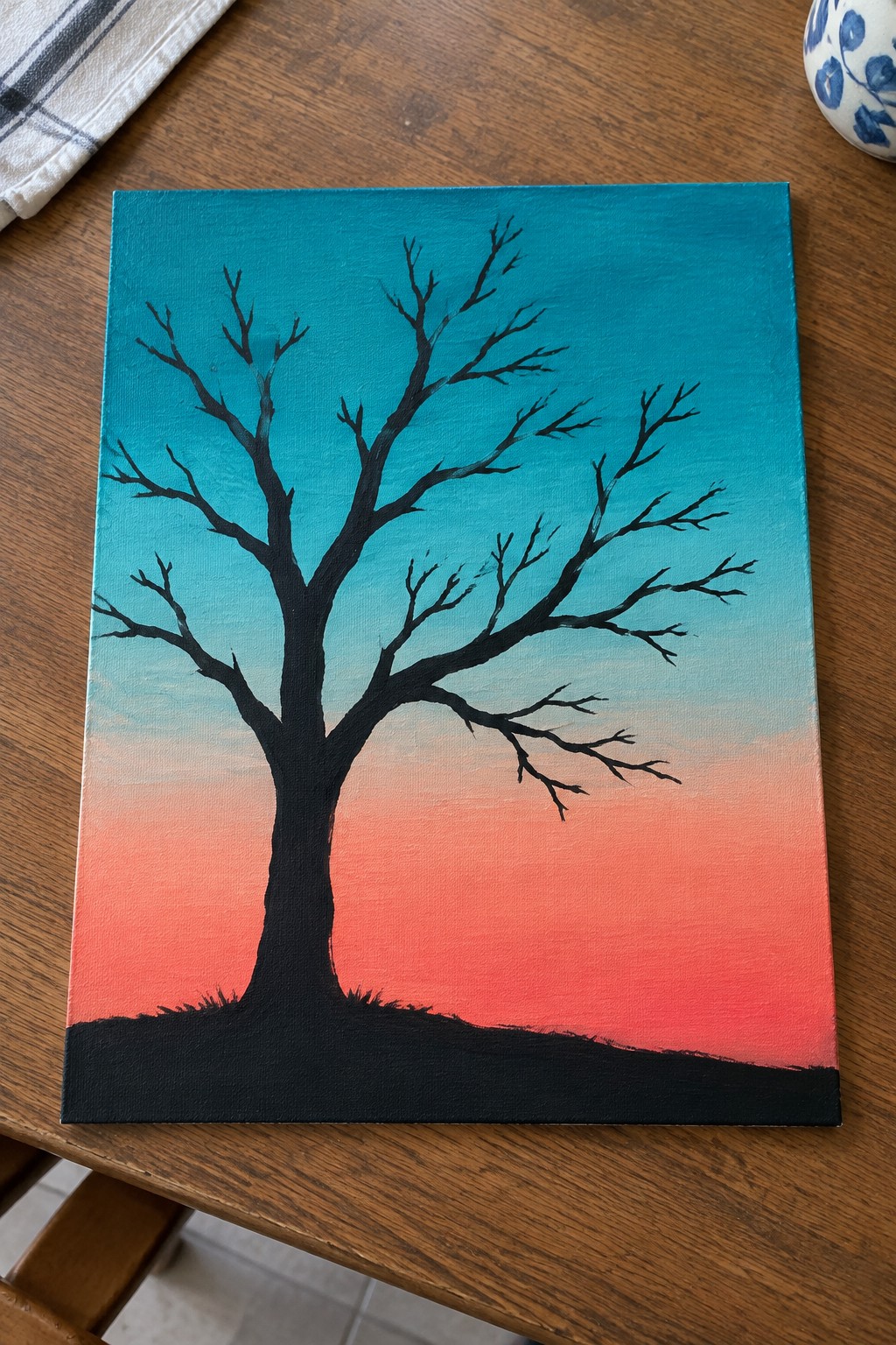 Black bare tree silhouette against teal to orange gradient sky on canvas
