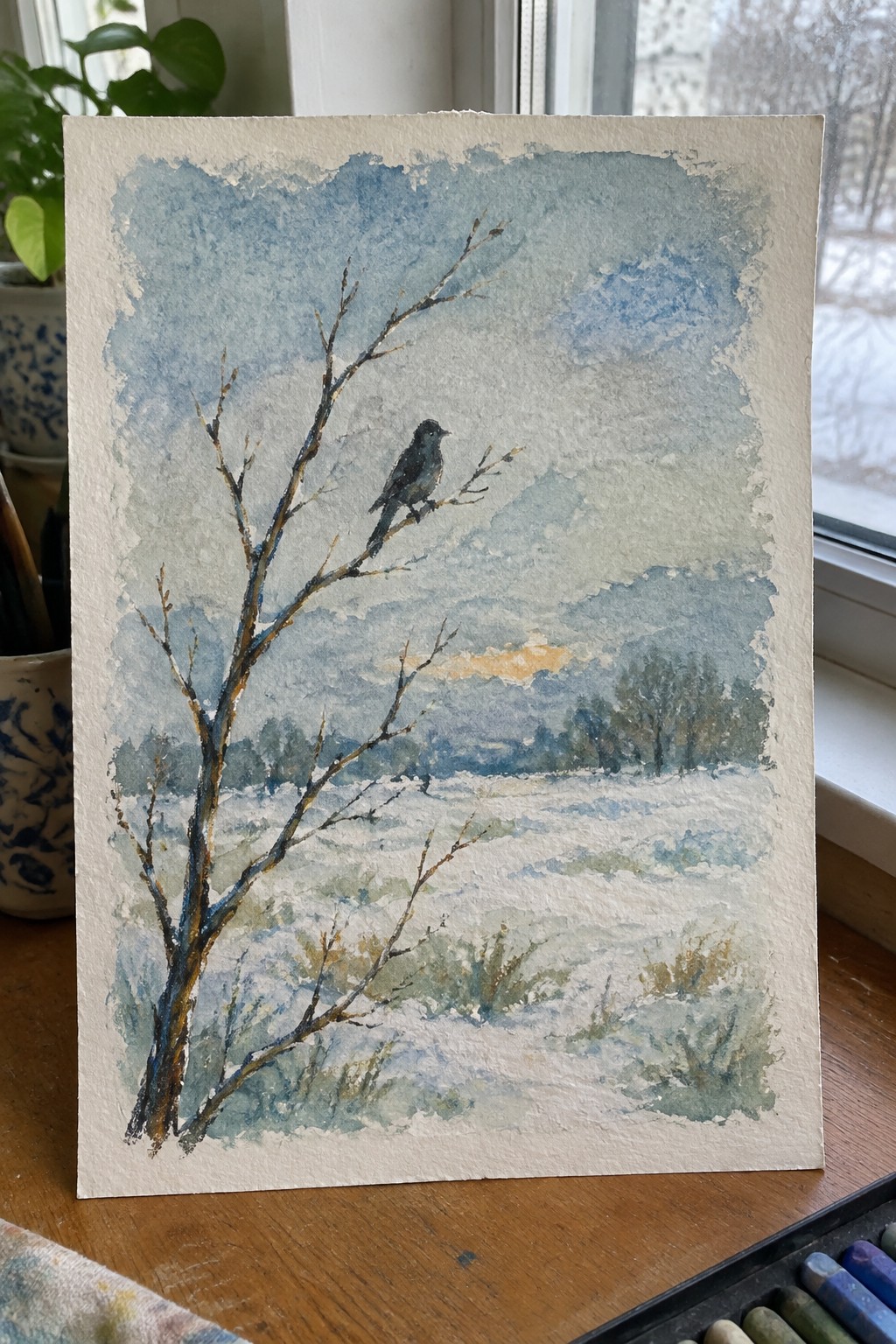 Watercolor of bird on bare tree in snowy field with blue cloudy sky and hills