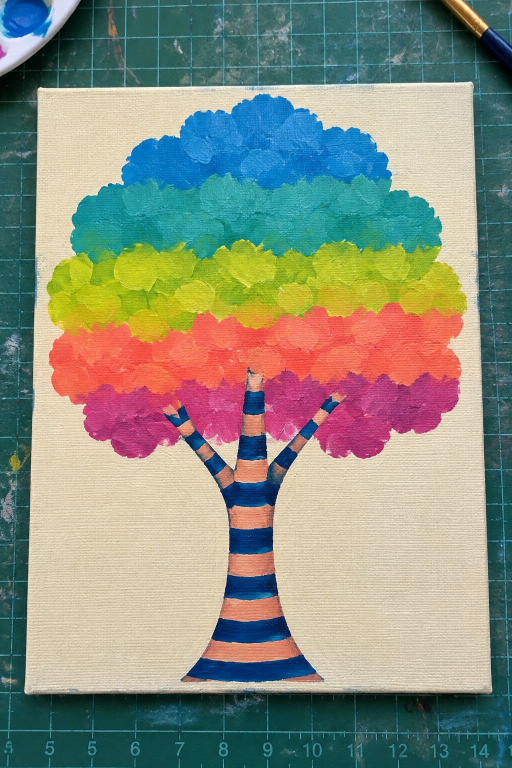 Rainbow tree painting with striped trunk on canvas surrounded by art supplies