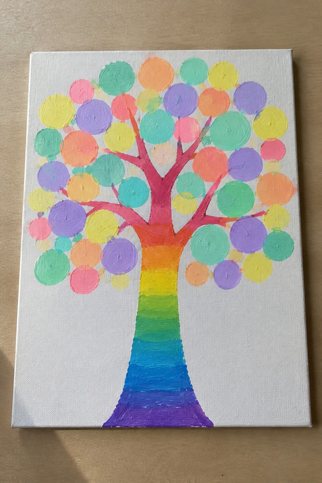 Vibrant rainbow tree painting with multicolored circular leaves on white canvas.