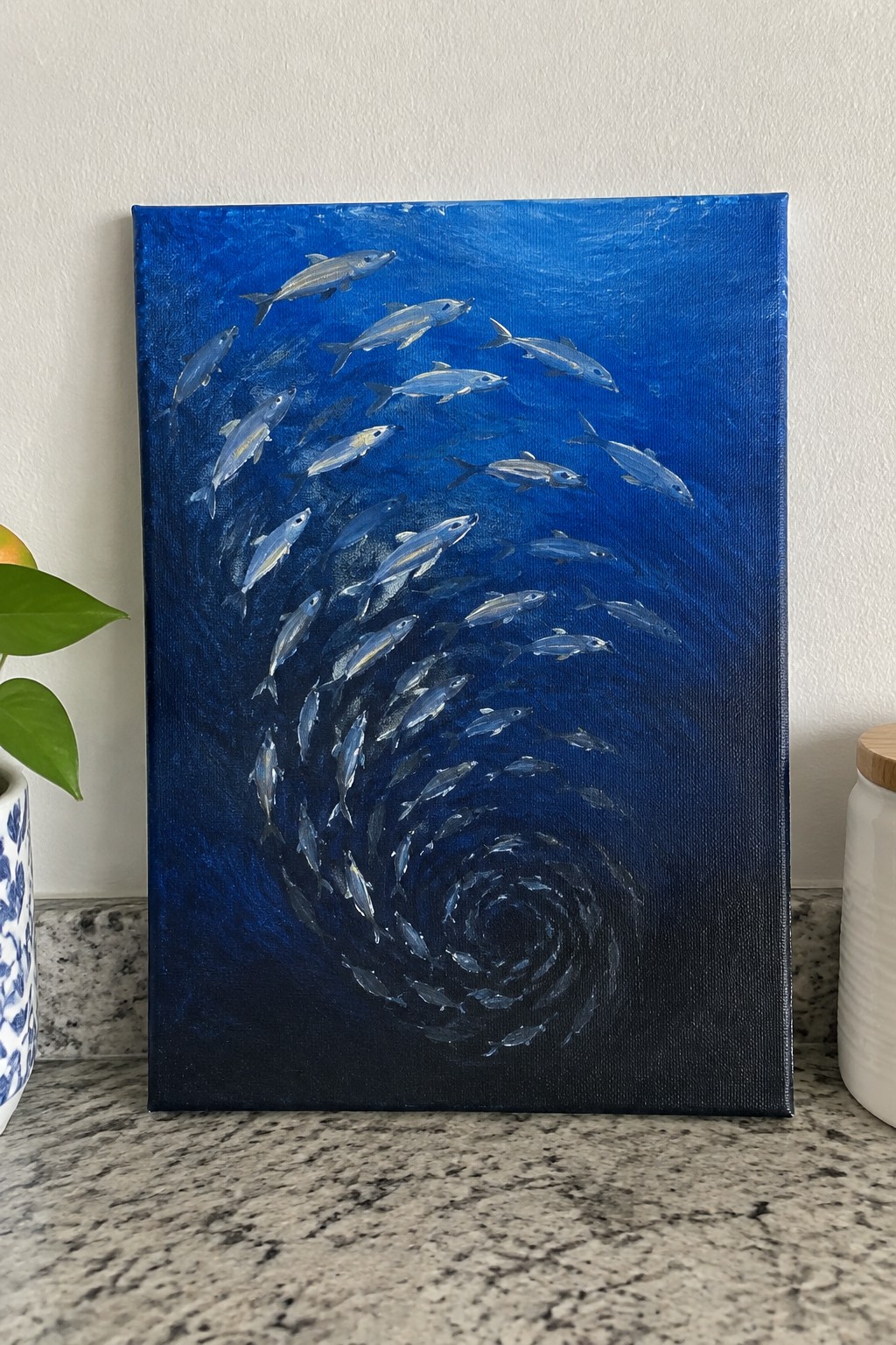 Painting of silver fish swirling in a spiral through deep blue water on canvas