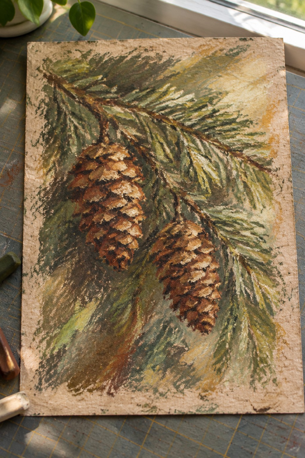 Painting of two brown pine cones hanging from a pine branch with green needles on textured paper.