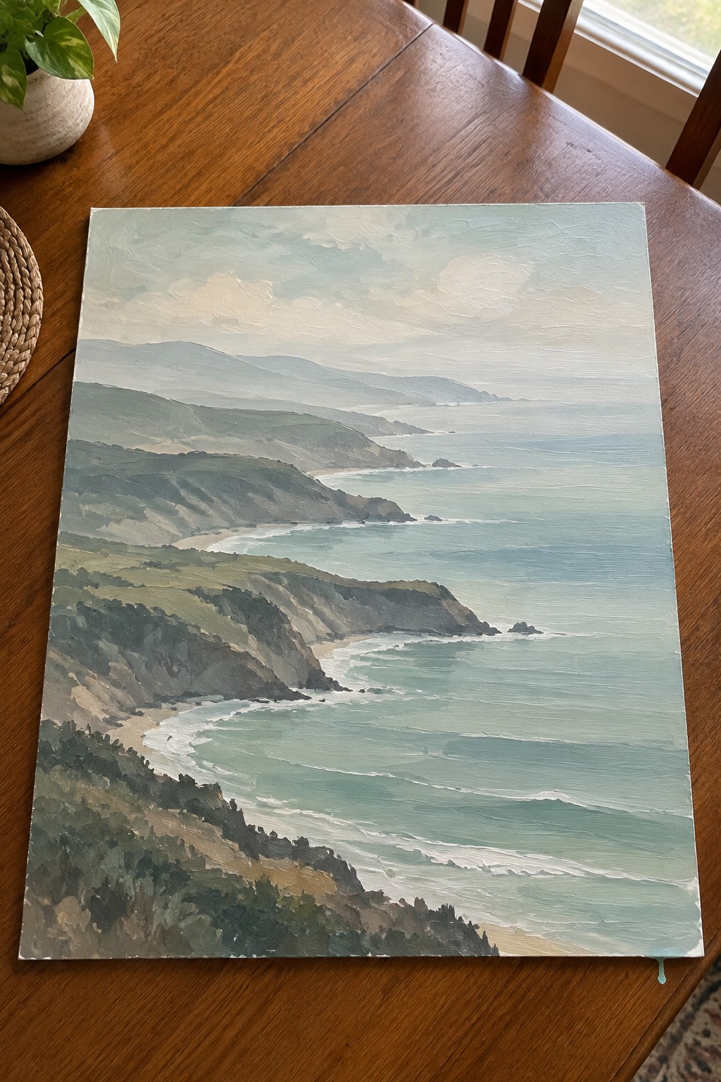 Coastal landscape painting with green cliffs, turquoise waves on wooden table