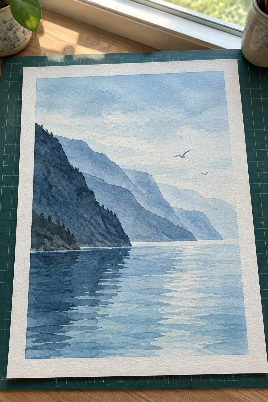 Blue watercolor of layered mountains reflected in calm lake with two birds overhead