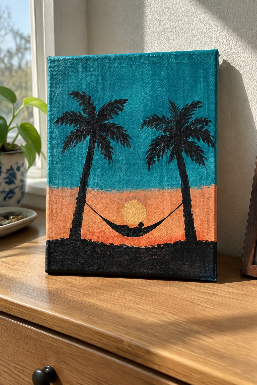 Silhouetted palm trees and hammock with person against orange sunset on teal sky