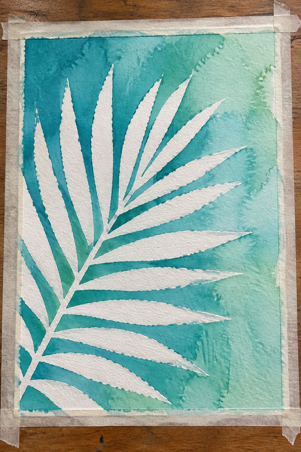 White palm frond silhouette on teal-green watercolor wash, taped to wood
