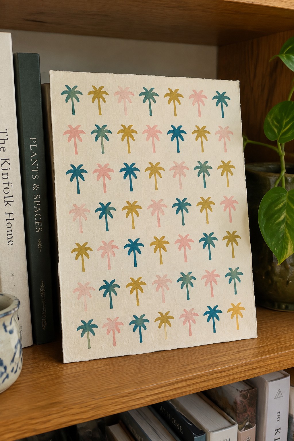 Colorful palm tree pattern on handmade paper atop wooden bookshelf with books