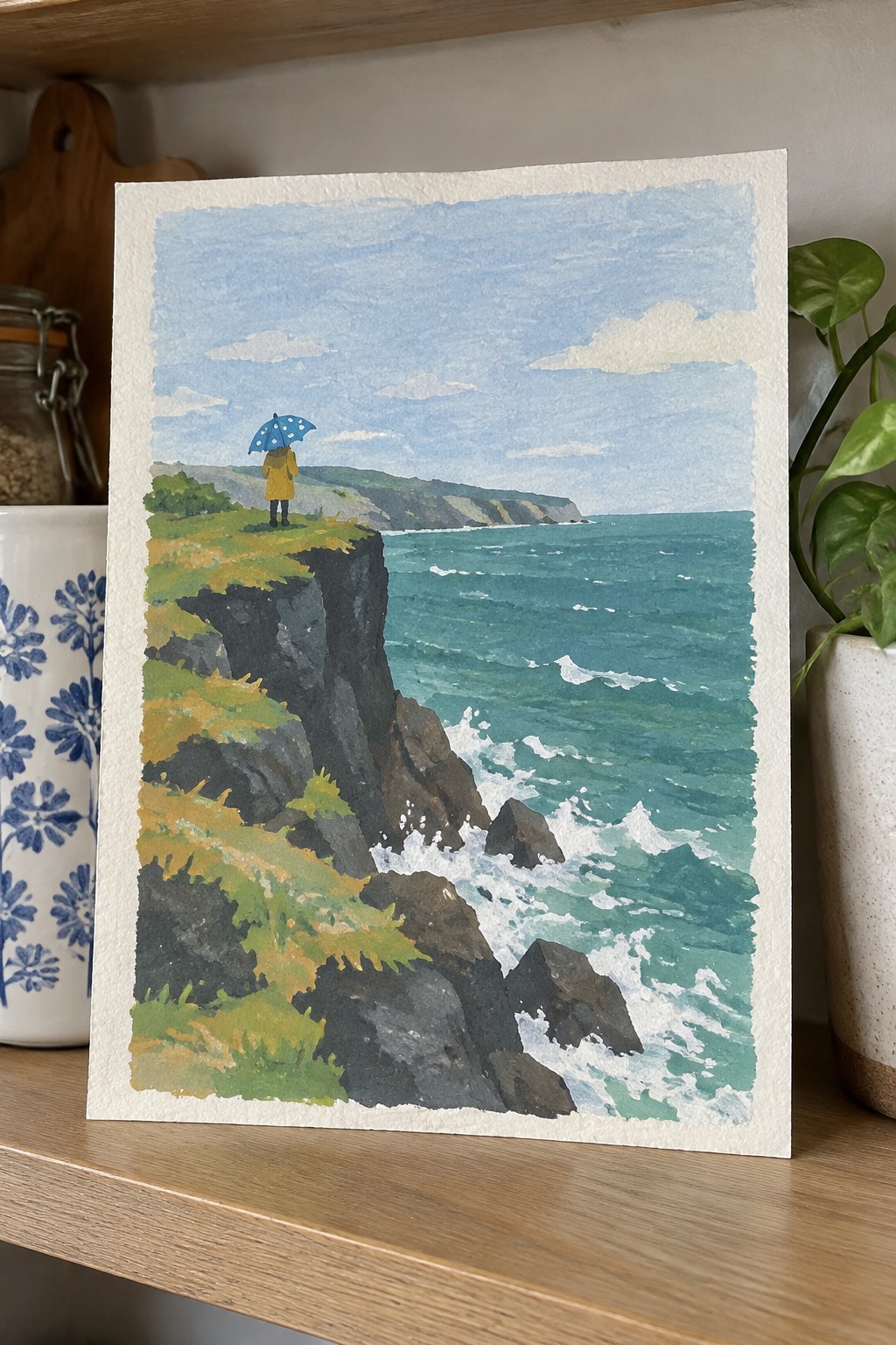 Watercolor of yellow-coated figure with polka-dot umbrella on cliff above crashing teal waves