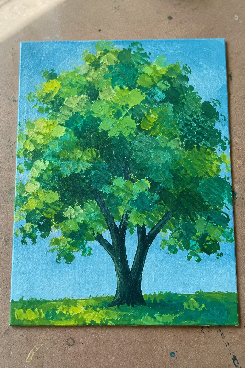 Impasto painting of large tree with thick dark trunk and vibrant green foliage on blue sky