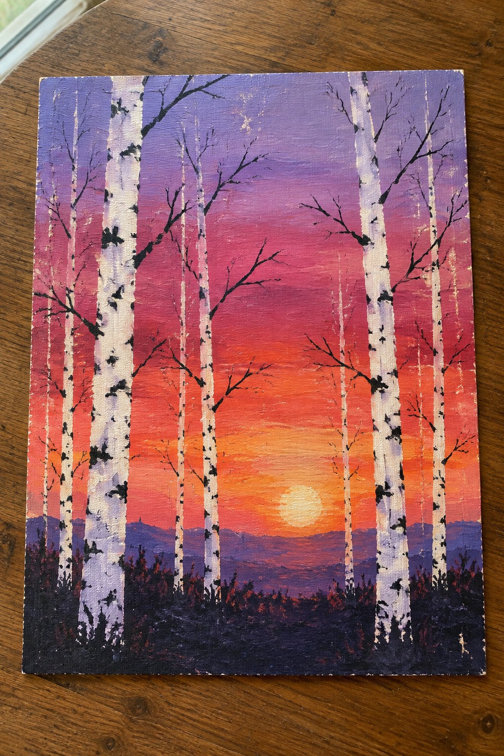 White birch trees before vibrant purple-pink-orange sunset sky with low sun and mountains