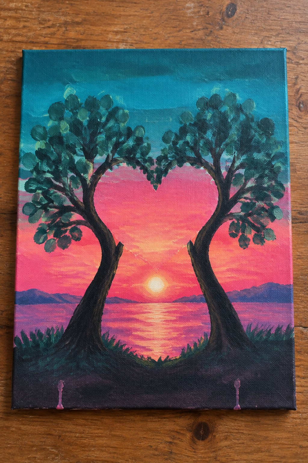 Two trees forming a heart shape over a pink sunset reflecting on water with mountains