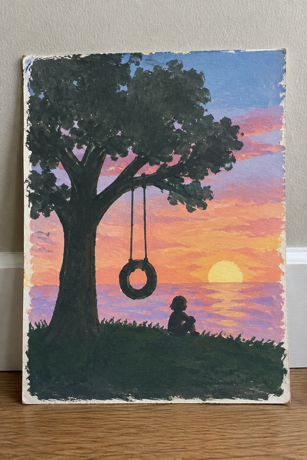 Child silhouette rests near tire swing on tree at vibrant ocean sunset painting