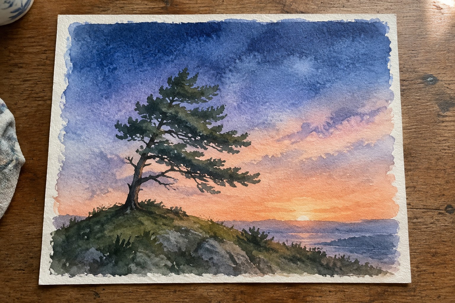 Watercolor of lone pine tree on cliff at sunset over calm waters.