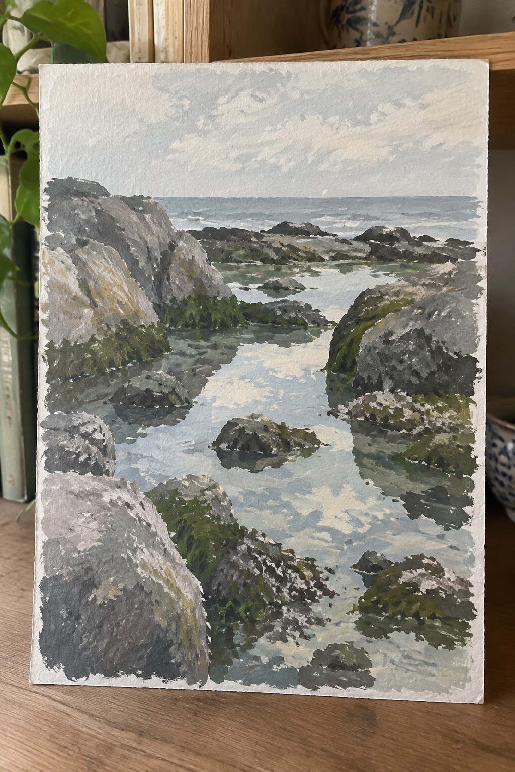 Watercolor seascape of rocky coastline, green moss, and reflective blue tidal pools.
