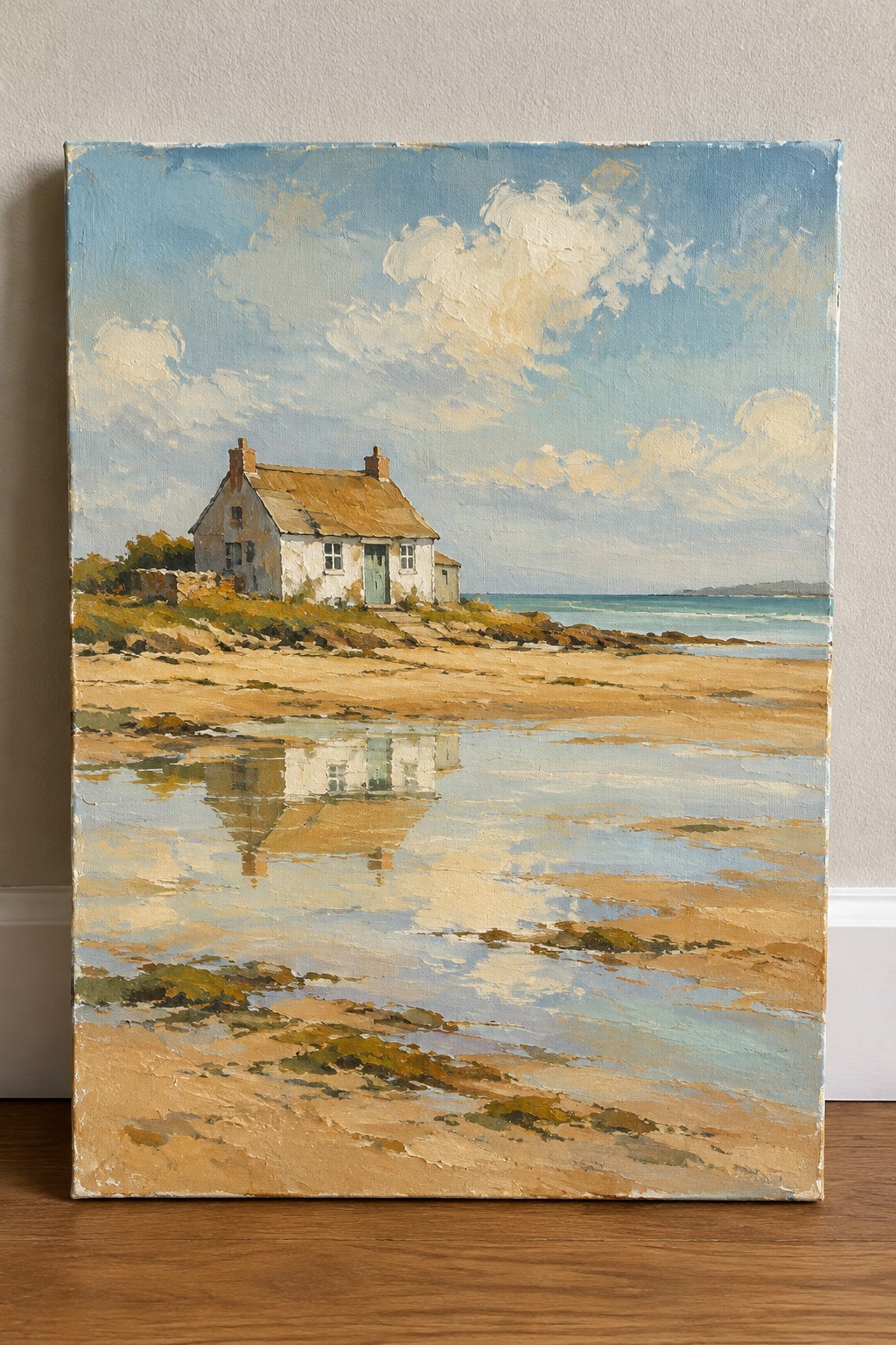 Oil painting of white cottage on sandy beach with puddles reflecting blue sky and sea.