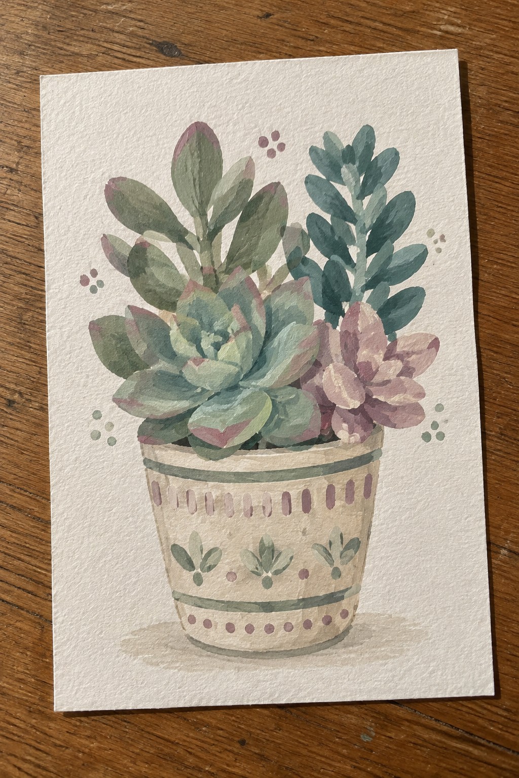 Watercolor painting of assorted succulents in a patterned beige pot on wood