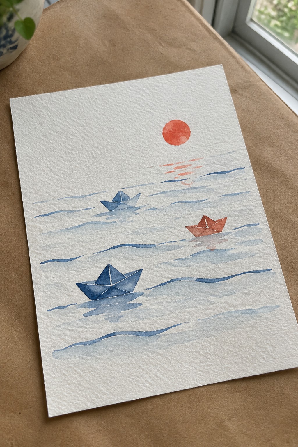 Watercolor painting of three paper boats on blue waves with a red sun above.