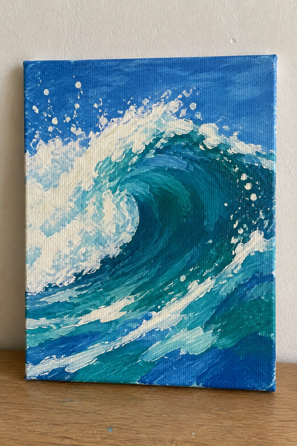 A small square canvas shows a curling ocean wave in shades of blue and teal with white foam and spray against a solid blue background.