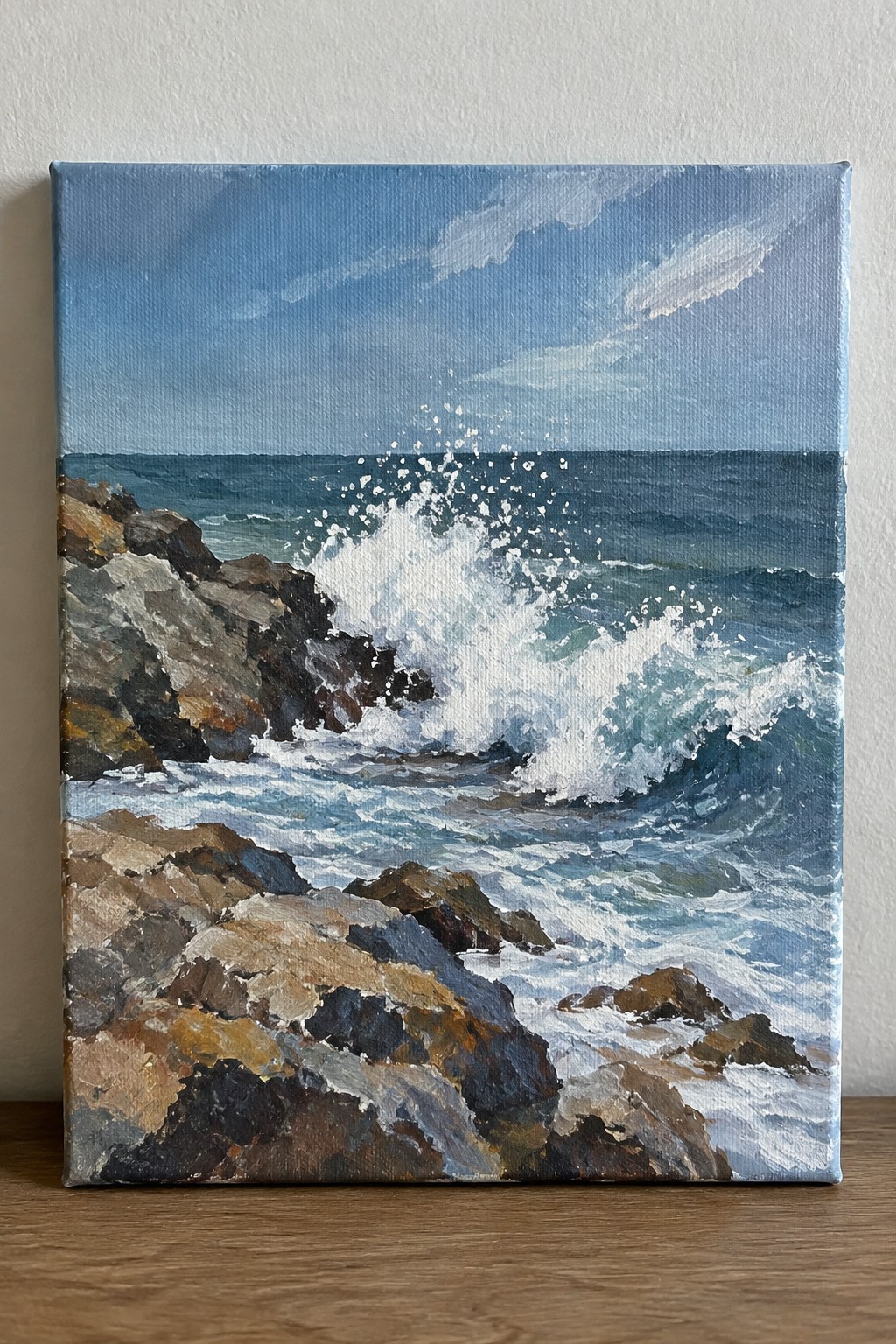 Oil painting of white waves crashing on brown rocks under blue sky.