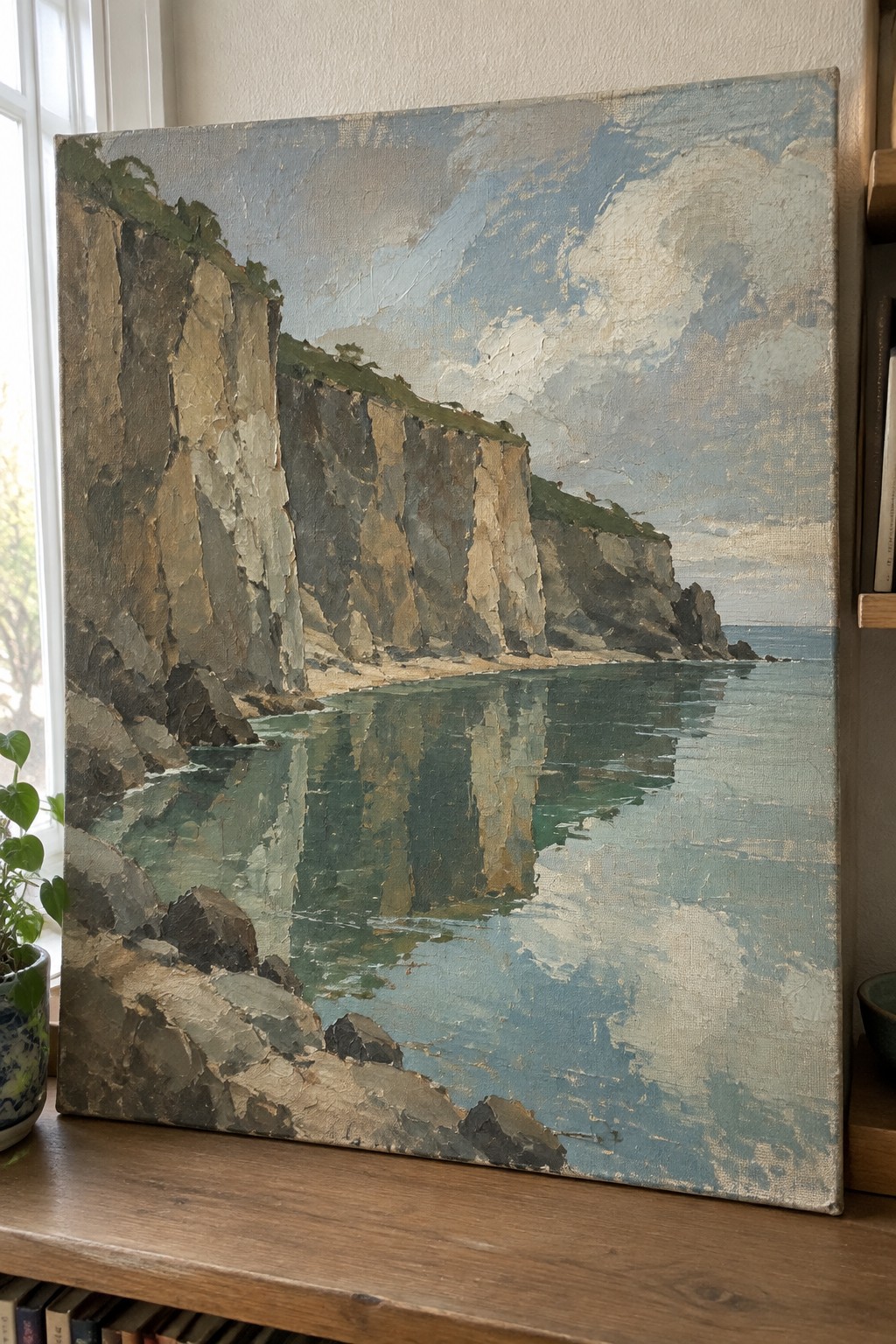 An oil painting of steep rocky cliffs reflected in calm blue-green ocean water under a cloudy sky.