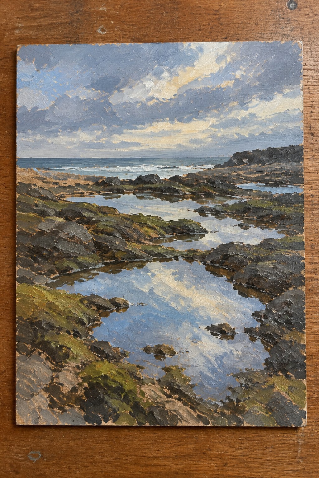 Rocky shoreline with reflective tide pools under cloudy blue sky and ocean waves