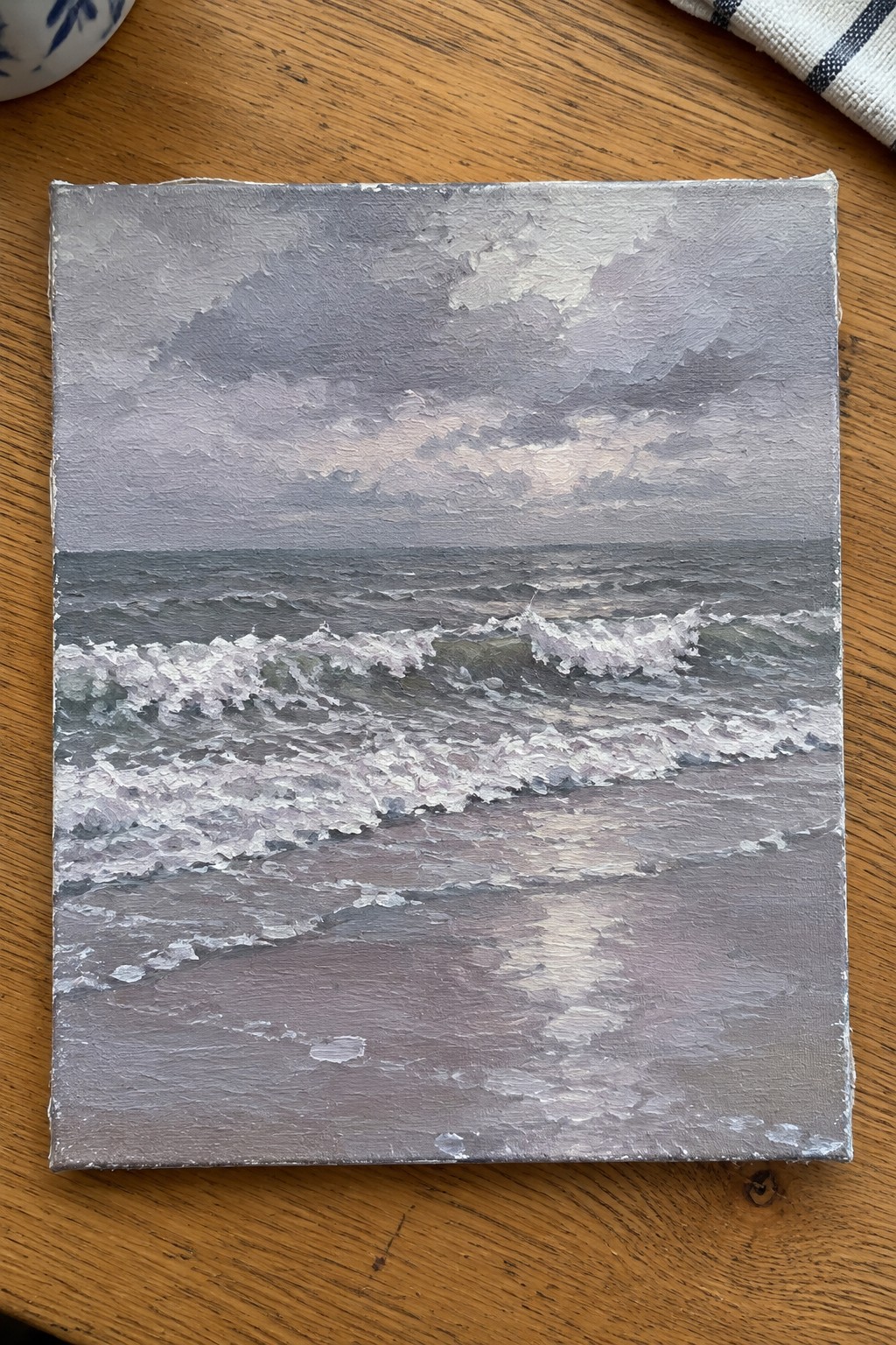 Textured painting of foamy waves crashing on beach under cloudy gray sky on wood