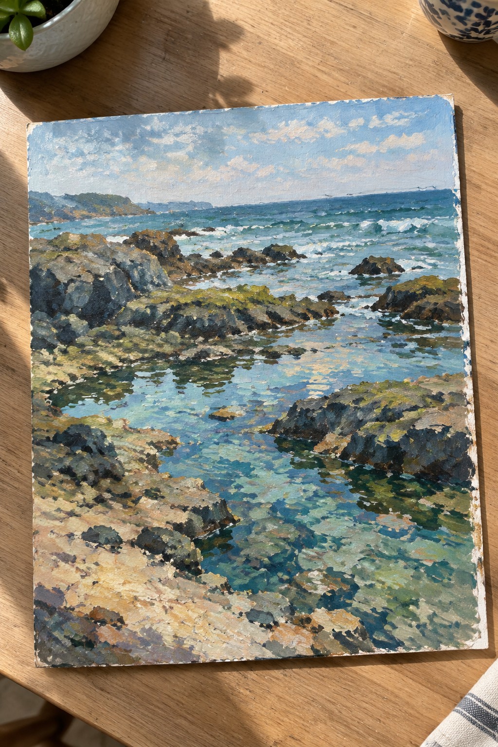 Vibrant seascape painting of rocky turquoise coastline with waves under blue sky on wood table