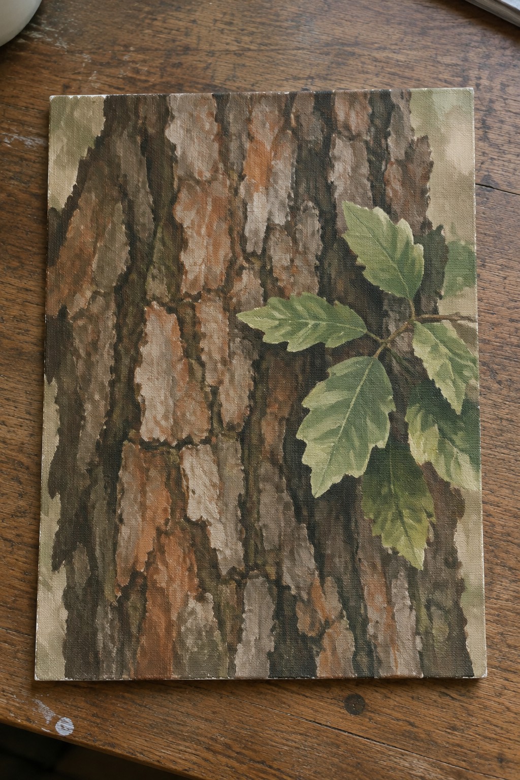 Painting of textured brown tree bark with green leaves on wooden table