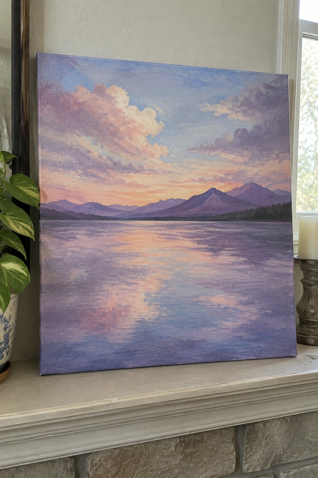Mountain landscape painting at sunset in purple hues on mantel next to plant and candle.