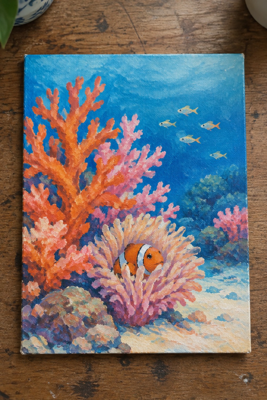 Colorful coral reef painting with orange clownfish amid pink coral and small yellow fish.