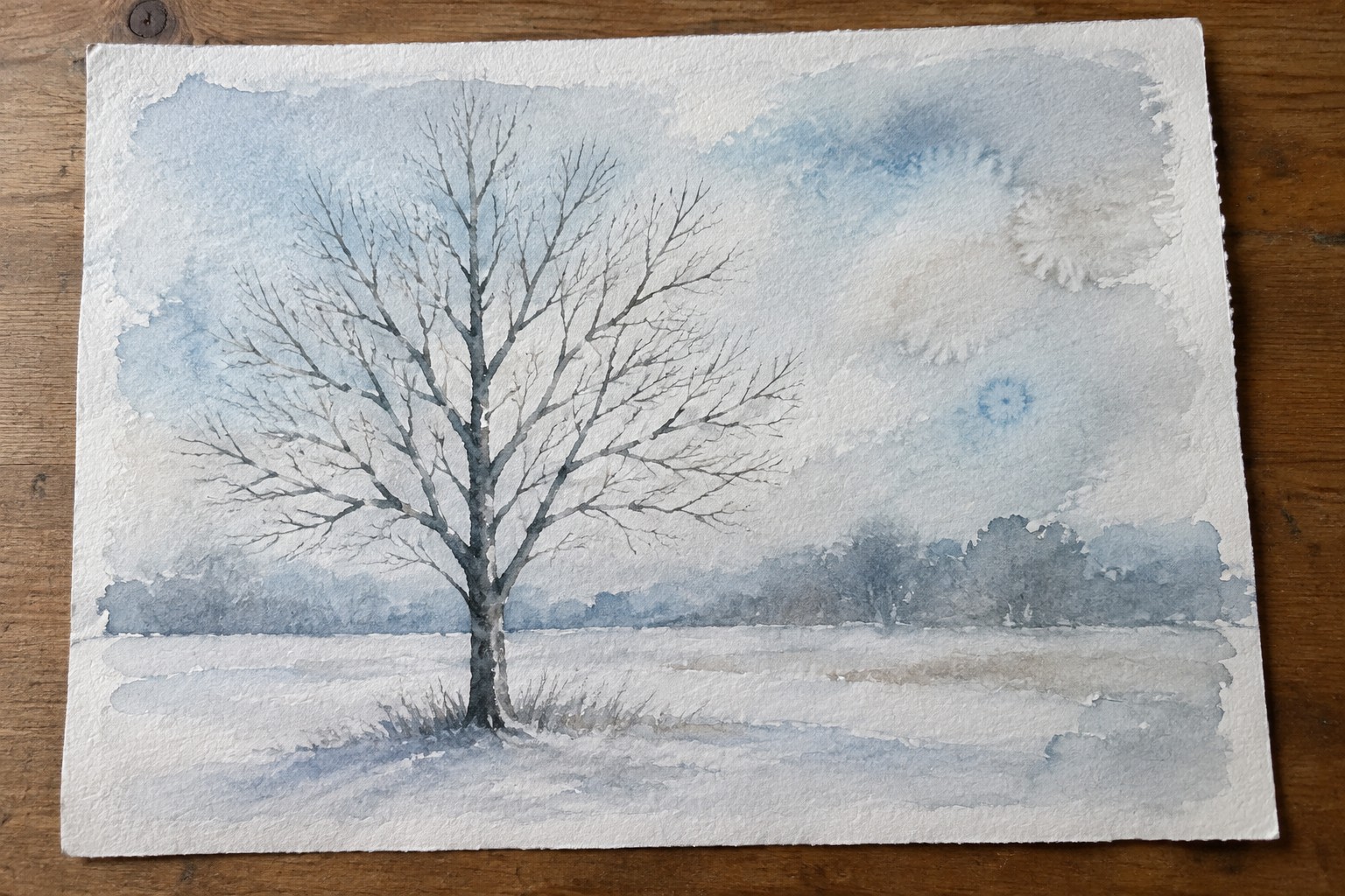 Watercolor of bare tree in snowy field with misty hills under pale blue sky
