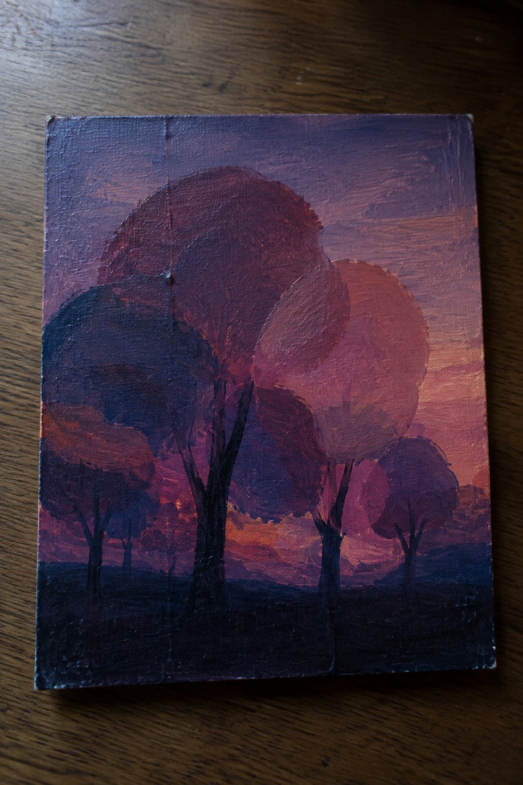 Oil painting of dark trees silhouetted against purple-orange sunset sky on canvas.