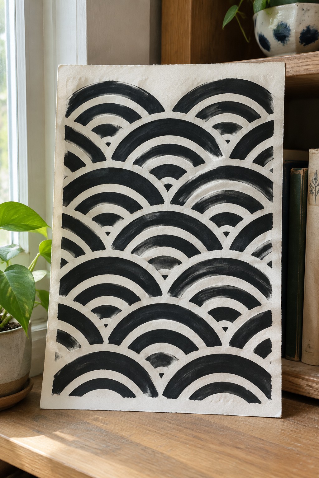 Black geometric arc pattern on textured paper atop wooden table with plants nearby.
