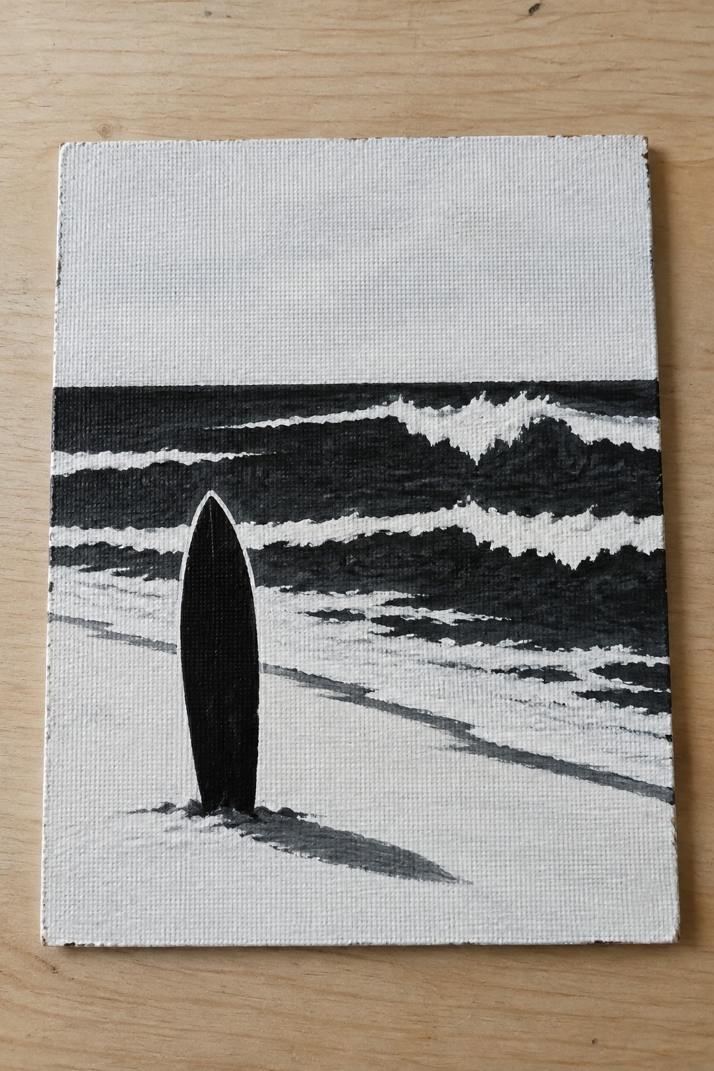 Black surfboard upright on beach with stylized black-and-white ocean waves in painting